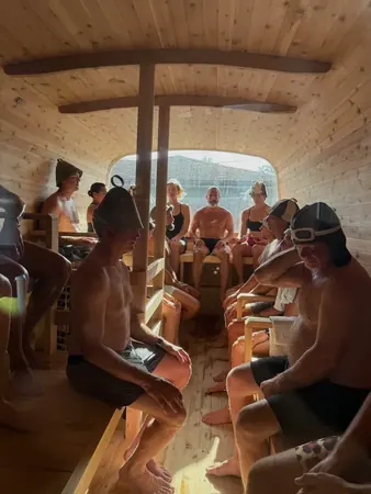 Participants seated along the benches of a cedar sauna with the door open to daylight