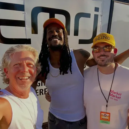 Keith with two collaborators in front of the EMRJ Wellness banner at an event