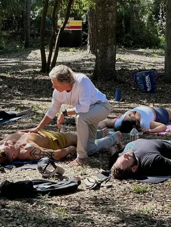An outdoor breath session in the trees with participants lying on the ground as Keith moves between them