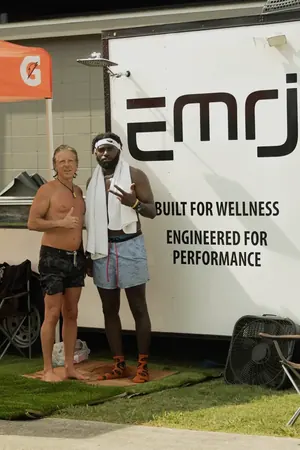 Keith and a participant beside the EMRJ Wellness wall reading built for wellness, engineered for performance